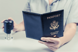 A border security agent holding a stamp in one hand while reading a person's passport in the other.