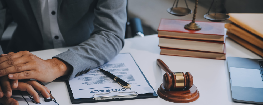 An immigration lawyer in an office resting his hands on a desk and presenting a clipboard to a client.