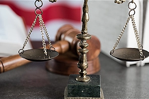 A gavel and scales of justice resting on a table with the American flag in the background.